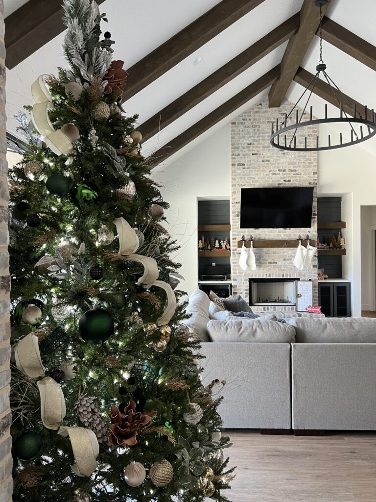 A beautifully decorated Christmas tree with green and gold ornaments in a living room