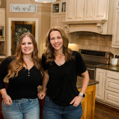 "Two women smiling in a cozy kitchen setting with rustic decor."